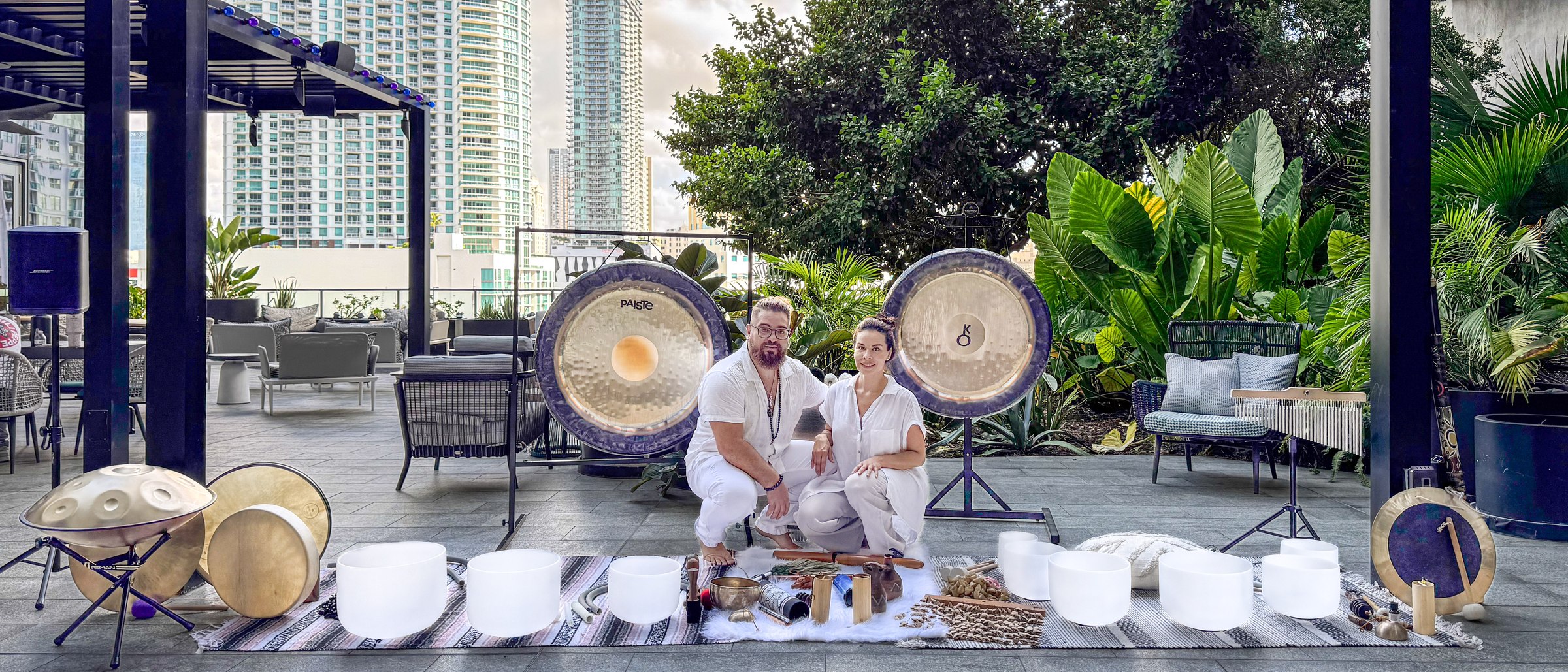 Karina and Juan seated in white before two gongs and a row of crystal bowls