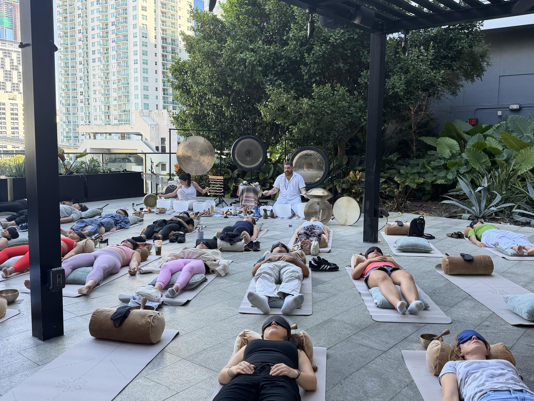 People resting on mats on a terrace among Brickell towers, gongs at the front